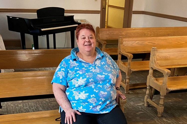 Linda, a resident of Project HOME sitting on a wooden pew in Kate's Place, Project HOME's largest residence in Center City. 